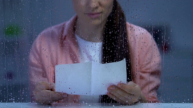 沮丧寂寞的女士坐在雨窗后读信，思念家人视频素材