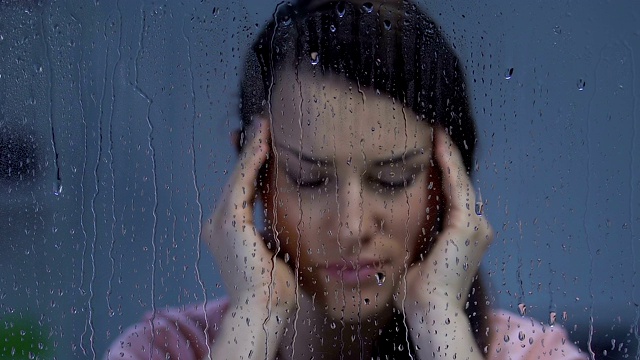 妇女患偏头痛，在雨窗附近揉太阳穴，对天气敏感视频素材