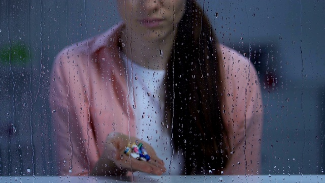 孤独的生病的女人拿着药靠近下雨的窗户看着相机视频素材