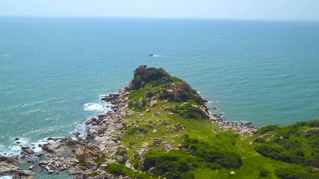 碧海绿岛上的岩石悬崖和空中的帆船景观。无人机观看悬崖上的岩石海岸的绿色岛屿在海洋和船舶航行在地平线上视频素材