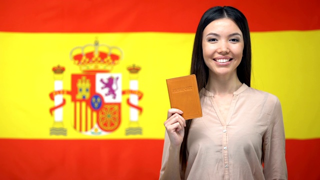 微笑的亚洲女孩拿着护照西班牙国旗背景，国籍视频素材