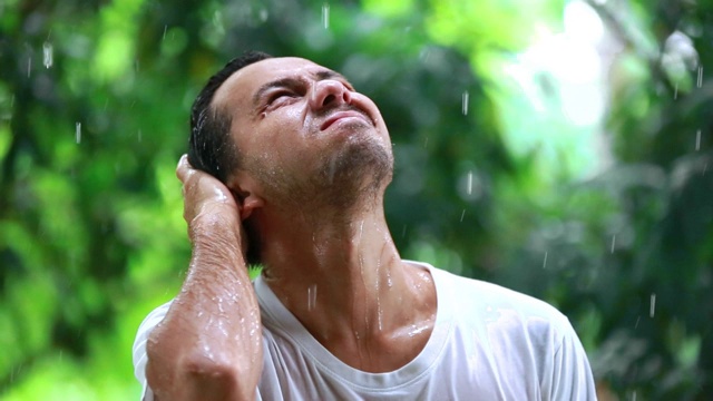 年轻人不开心的站在雨中，一个悲伤的人在雨中的肖像，糟糕的暴风雨下雨的天气概念视频素材画面1