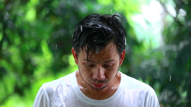 年轻人不开心的站在雨中，一个悲伤的人在雨中的肖像，糟糕的暴风雨下雨的天气概念视频素材画面2