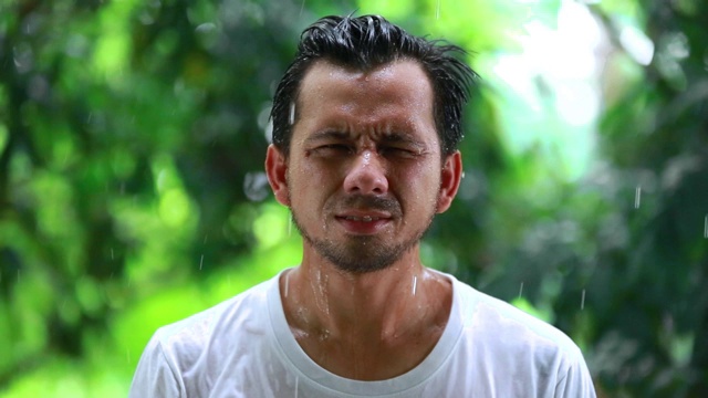 年轻人不开心的站在雨中，一个悲伤的人在雨中的肖像，糟糕的暴风雨下雨的天气概念视频素材画面3