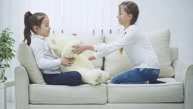 两个可爱快乐的女孩玩着泰迪熊，重新调整它的领结，拥抱着她们的毛绒朋友。视频素材