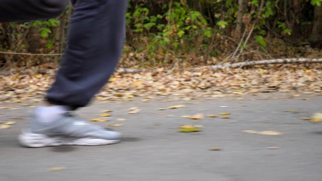 初秋，在森林附近的道路上奔跑的运动男子的脚。年轻运动员的双腿在大自然中沿着小径快速奔跑。强壮的家伙在户外慢跑。健康积极的生活方式。低的观点视频素材