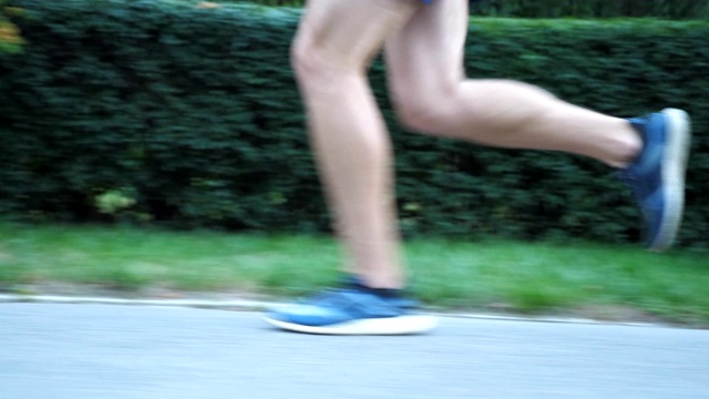 夏日里，在人行道上奔跑的运动男子的脚。年轻运动员的双腿在自然的道路上快速奔跑。强壮的运动员在户外慢跑。健康积极的生活方式。低的观点视频素材