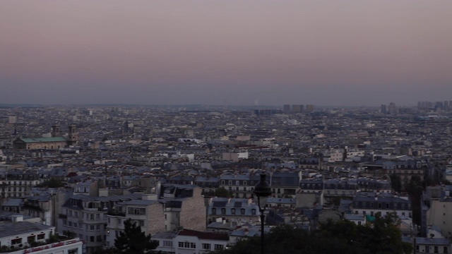 从蒙马特高地上鸟瞰巴黎的美景，一天结束时巴黎的天空是蓝橙色的。潘向左的老建筑，灯柱，摩天大楼。视频素材