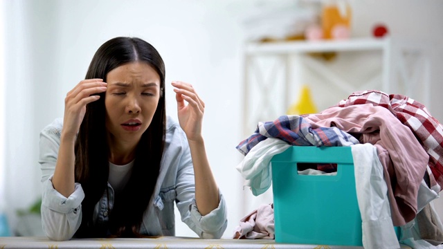 沮丧的家庭主妇看着洗衣篮里满满的衣服，劳累过度视频素材