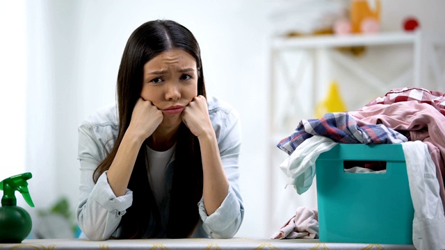 心烦意乱的家庭主妇看着摄像机，桌上的洗衣篮里装满了衣服视频素材