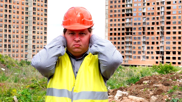 年轻英俊的建筑工人害怕(男人用手捂住耳朵)-建筑工地视频素材