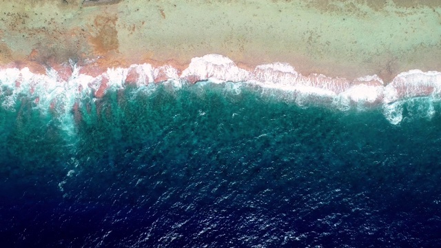 无人机鸟瞰图海浪撞击珊瑚礁上的热带海滩。一半是蓝色的海浪，一半是太平洋的海滩和珊瑚。海浪很大。旅行热带概念- 4K视频素材