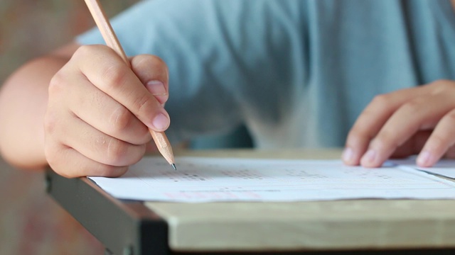 教育考试在大学或高中的概念:手持铅笔的学生测试试卷上的答案，在校园教室填写试卷。知识学习的概念视频素材