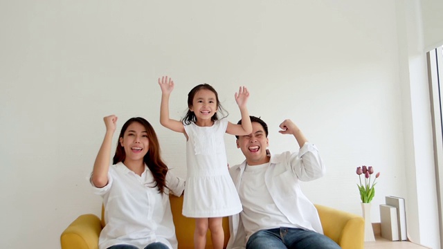 幸福的亚洲家庭一起在家看电视。三岁的爸爸、妈妈和女儿都喜欢看电视。慢动作120帧/秒视频素材画面1