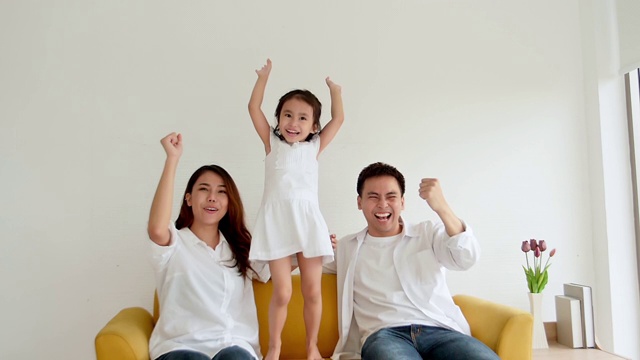 幸福的亚洲家庭一起在家看电视。三岁的爸爸、妈妈和女儿都喜欢看电视。慢动作120帧/秒视频素材画面3