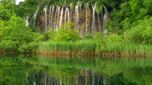 克罗地亚Plitvice湖国家公园。水流如瀑布般从岩石中流下，在丰富的绿色植物中，反映在前景中的普利特维茨湖之一。UHD视频素材