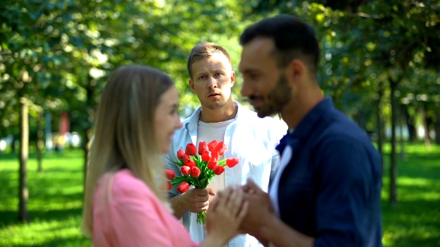 失望的男人拿着花看着他的女朋友和另一个男人接吻视频素材