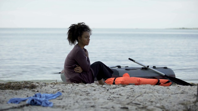 坐在海边小船旁的冻僵的少女，海难中的难民幸存者视频素材