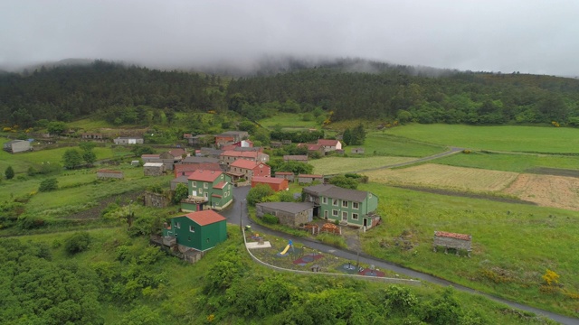 航拍:在多雾的天气里，无人机在山区村庄的传统房屋和绿色农田上移动——西班牙加利西亚视频素材