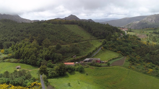 航拍:无人机降落在乡村公路上，在绿树成荫的风景中，群山映衬着多云的天空。西班牙加利西亚视频素材