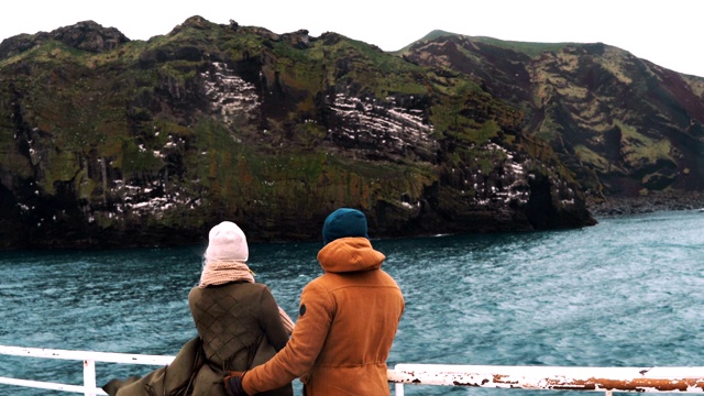 年轻夫妇一起坐船旅行的后视图。男人和女人站在船的野猪上，看着山。视频素材