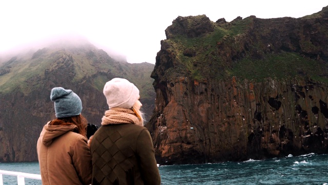 两个乘船旅行的女人一起站在船上。女性拿着相机在水中拍摄山。视频素材