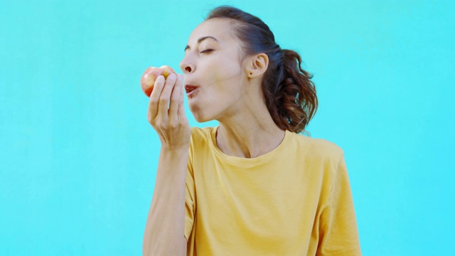 美丽的微笑女孩吃着新鲜的成熟的美味的黄红苹果，摆姿势在鲜艳的青色背景视频素材