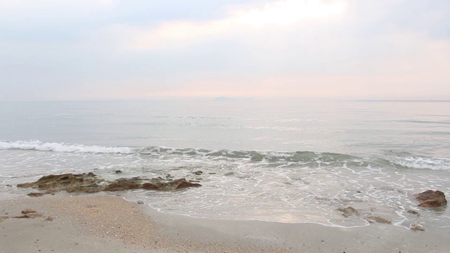 阳光在早晨随着海浪慢慢地溅在沙滩上，岩石上长满了苔藓。热带海滩宁静的田园风光。视频素材