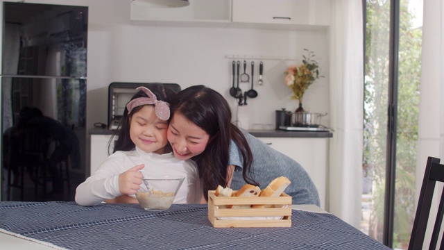 日本亚裔家庭在家里吃早餐。亚洲妈妈和女儿感到愉快的谈话在一起，而吃面包，玉米片谷物和牛奶碗在厨房的桌子上在早上。缓慢的运动。视频素材