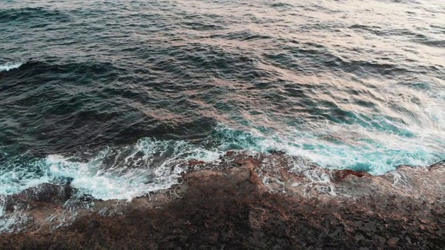 无人机沿着布满黑色石头的海岸飞行，巨大的海浪撞向悬崖视频素材