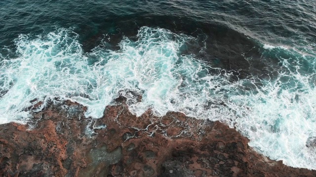 无人机俯视图暴风雨的海浪打击和蔓延在岩石上。白色和蓝色的海浪飞溅视频素材