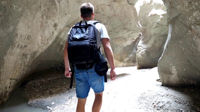 一个背着背包的年轻人穿过狭窄的峡谷。男性徒步旅行者探索岩石峡谷和欣赏风景。旅行或主动休息的概念。慢动作后景特写视频素材