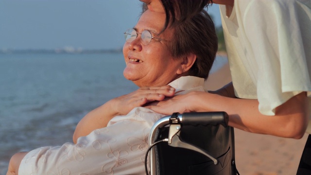 微笑快乐的亚洲资深母亲与她的成年女儿拥抱在海滩上的肖像。快乐的女儿在一起的时候牵着看护者的手。老年假期，假期，关怀，退休，家庭观念，不同能力的旅行视频素材画面3