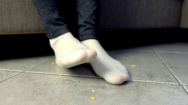 一个女人坐在沙发上吃东西，把玉米片弄碎在地上。腿和地板特写。视频素材画面3