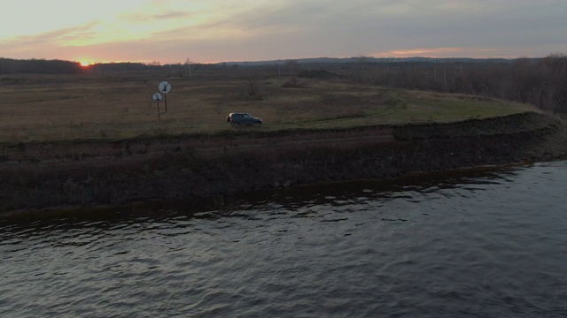 黑色越野车行驶在河岸上的金色日落景观。跨界车沿着海岸在傍晚的阳光海边行驶。视频素材