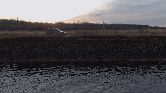 一辆黑色的汽车在海边行驶在金色的夕阳下。在傍晚的阳光下，越野车沿着海边行驶。视频素材