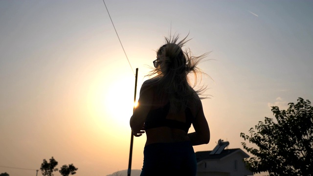 活泼的女孩慢跑在乡村道路与日落的背景。晚上在户外运动的年轻女性。女运动员在做跑步训练。健康生活方式的概念。后视图视频素材