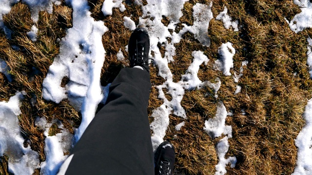 视角男性脚穿靴子踏过雪地。早春时节，年轻的徒步旅行者的双腿在雪地上行走。寒假或假期的概念。特写慢镜头视频素材