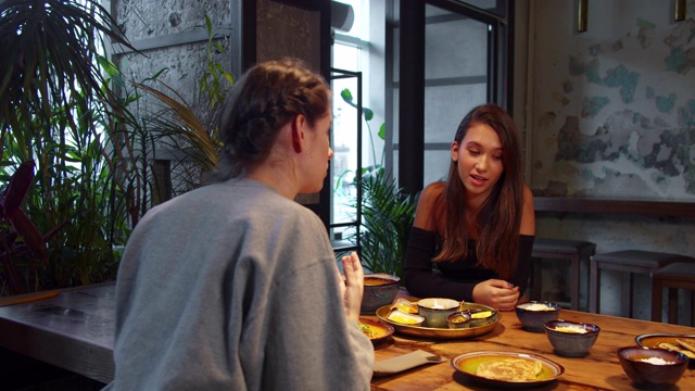 两个女孩在吃午饭时，她们坐在一起，其中一个讲述桌上的食物视频素材