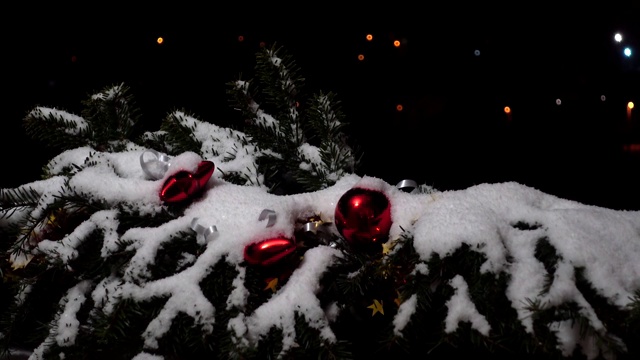 圣诞树的树枝上装饰着雪下的玩具。以夜城为背景，在夜晚拍摄。视频素材画面3