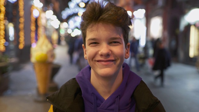 漂亮的少年微笑，看着相机在繁忙的城市街道与城市灯光在晚上。UHD 4 k视频素材画面2