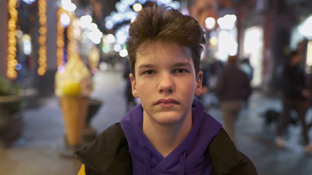 漂亮的少年微笑，看着相机在繁忙的城市街道与城市灯光在晚上。UHD 4 k视频素材画面4