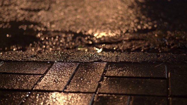 雨夜的城市街道，雨水在路灯下的人行道上流淌。视频素材