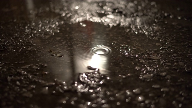 晚上，雨水落在人行道上的水坑里，街灯倒映在水中。视频素材