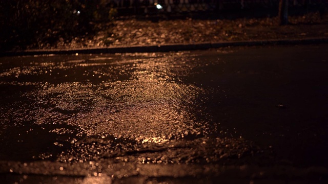 雨夜的城市街道，雨水在路灯下的人行道上流淌。视频素材