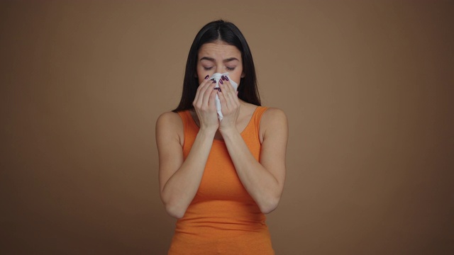 生病的黑发女人打喷嚏孤立的棕色背景视频素材