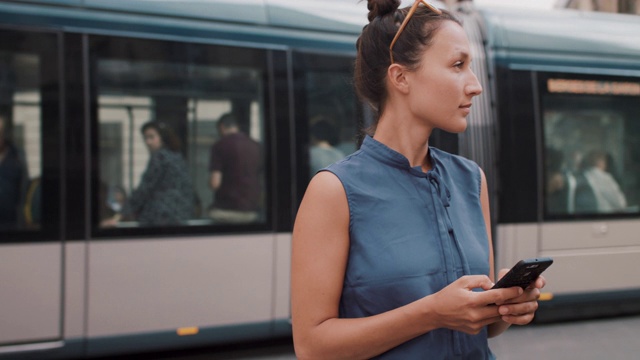 女人在城市街道上，手机和火车经过视频素材画面1
