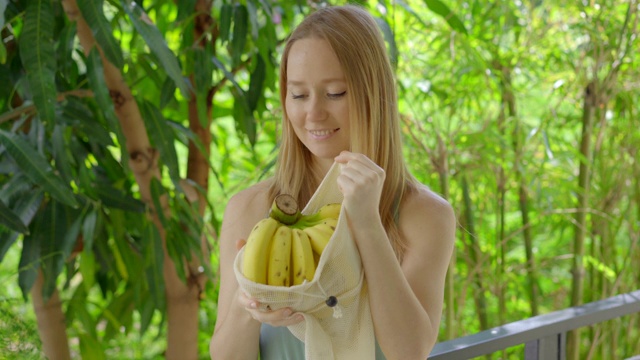 年轻女子把香蕉放进可重复使用的袋子里。减少塑料污染的概念。减少和重用视频素材