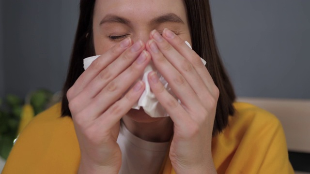 女孩打喷嚏。迷人的白种女人痒她的鼻子，她打喷嚏，看着镜头，用餐巾盖住她的嘴。感冒、流感、流鼻涕、急性呼吸道疾病等概念。近距离视频素材