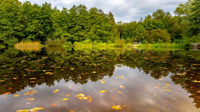 4K时间流逝秋天景观与湖泊。五颜六色的树叶公园在秋天。飘浮的树叶和云朵在水中倒映得完美无缺。德国。视频素材